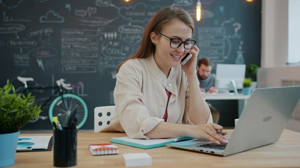 A bookkeeper at her desk on the phone, typing on a laptop